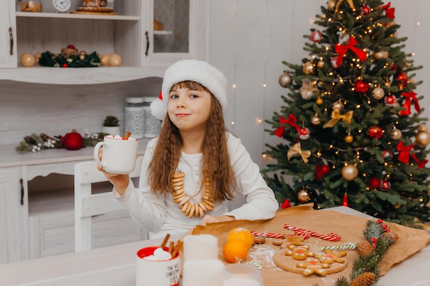 Mała dziewczynka w kapeluszu Świętego Mikołaja siedzi przy kuchennym stole.