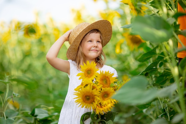 Mała dziewczynka w kapeluszu trzyma bukiet słoneczników na polu słoneczników