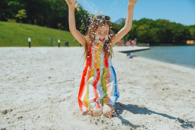 Mała dziewczynka w letniej sukience rzuca piaskiem na plażę letnie wakacje