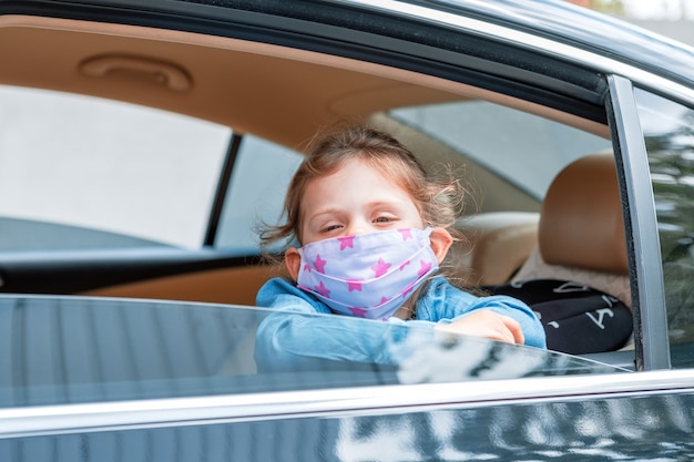 Mała dziewczynka w medycznej masce od samochodowego okno. Koronawirus lub covid-19 chroniący maskę higieniczną