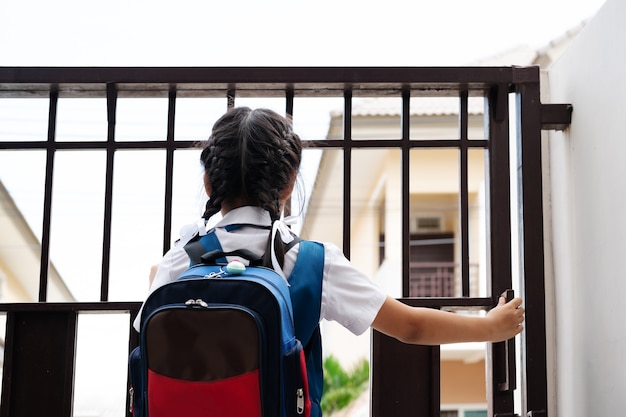 Mała Dziewczynka W Mundurze Otwiera Drzwi Dla Opuszczać Szkoła W Ranku Z Błękitnym Bac