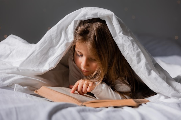 Mała dziewczynka w nowożytnej piżamie czyta książkę w domu w łóżku wysokiej jakości zdjęcie