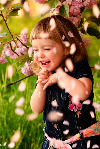 Mała dziewczynka w ogrodzie, pod drzewem sakura. Wiosenny deszcz płatków.