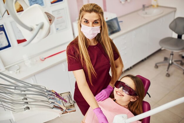 Mała dziewczynka w okularach ochronnych odwiedza dentystę w klinice Poczęcie stomatologii