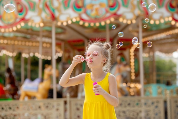 Mała dziewczynka w okularach przeciwsłonecznych latem dmucha w parku bańki mydlane