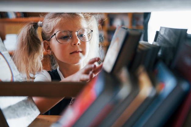 Mała Dziewczynka W Okularach Szukająca Książki W Bibliotece