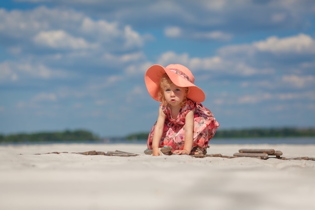 Mała dziewczynka w pięknej sarafnie bawi się w piasku na plaży.