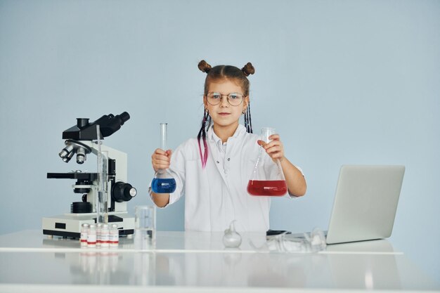 Mała dziewczynka w płaszczu gra naukowca w laboratorium za pomocą sprzętu