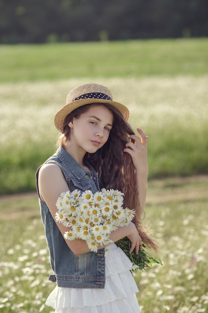 Mała dziewczynka w polu kwiatów daisy. Nastoletnia dziewczyna w kapeluszu i sukience cieszy się wiosną w stokrotkowym polu