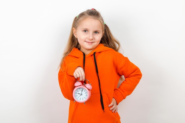 Mała dziewczynka w pomarańczowym garniturze trzyma budzik Pojęcie nadszedł czas, czas na szkołę