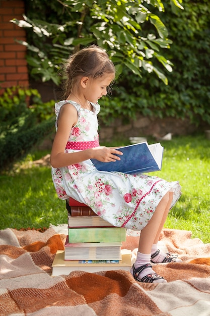 Mała dziewczynka w ślicznej sukience siedzi na stosie książek i czyta