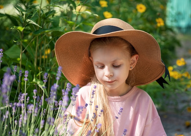 Mała dziewczynka w słomkowym kapeluszu otoczona lawendowymi kwiatami