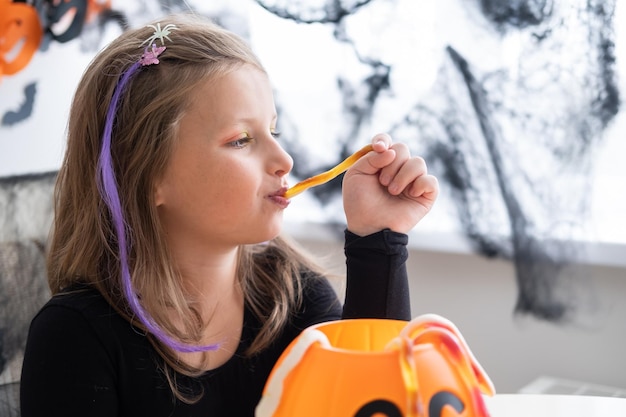 mała dziewczynka w stroju wiedźmy trzymająca dyniowego jacka z cukierkami, świętująca Halloween w domu