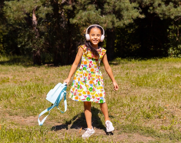 Mała dziewczynka w sukience i słuchawkach bawi się i skacze w parku na trawie.