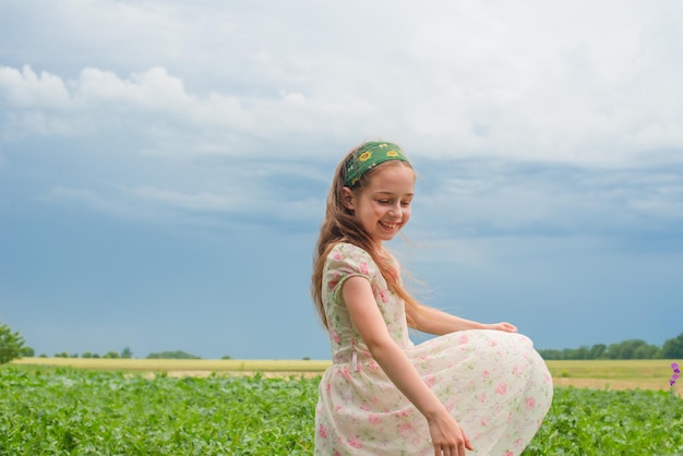 Mała dziewczynka w sukience w kwiaty na tle wiejskiej przyrody Radość dziecka