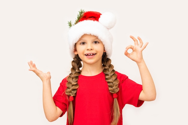 Mała dziewczynka w świątecznej czapce pokazuje znak OK.