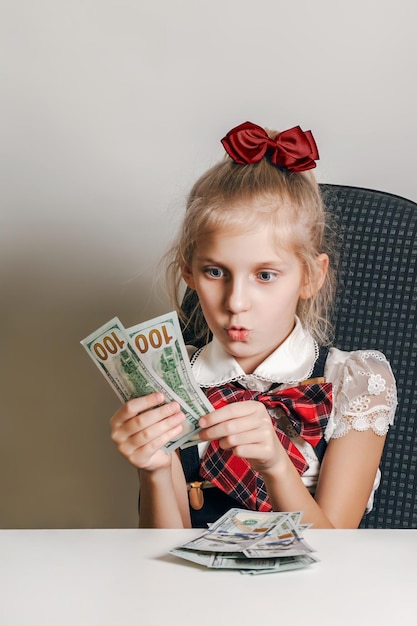 Mała dziewczynka w szkolnym mundurku patrzy na pieniądze ze zdziwieniem i podziwem