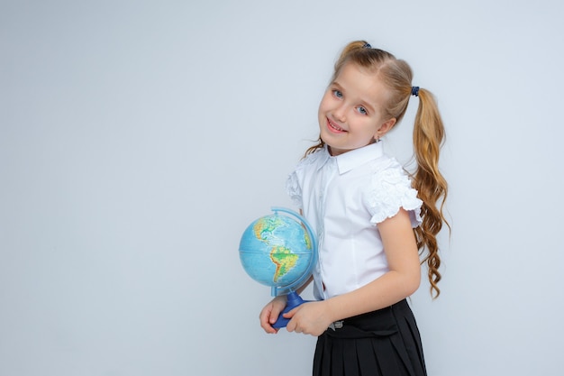 Mała dziewczynka w szkolnym mundurku trzyma w rękach kulę ziemską na białym tle