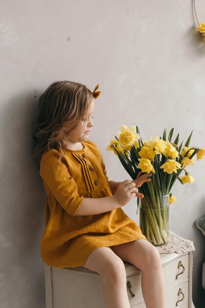 Mała dziewczynka w żółtej sukience z pięknym bukietem kwiatów narcyzów