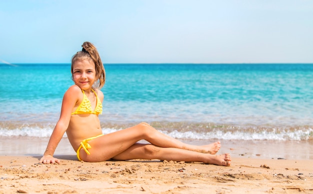 Mała dziewczynka w żółtym bikini siedzi na piasku plaży