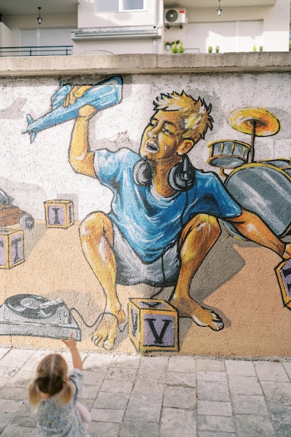 Mała dziewczynka wskazuje na graffiti chłopca z słuchawkami z samolotem z zabawkami na ścianie