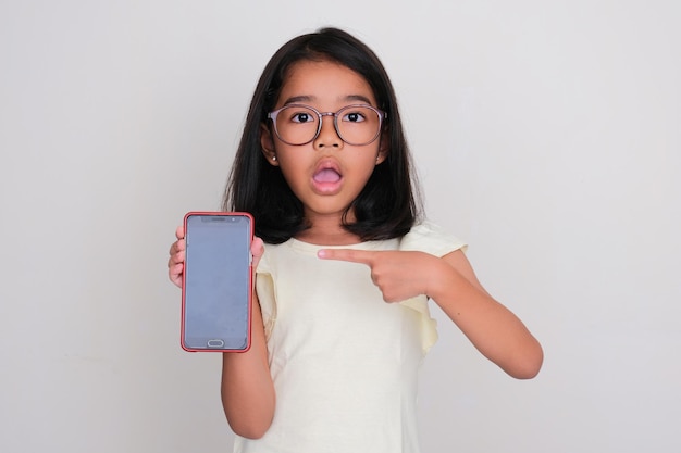 Mała Dziewczynka Wskazuje Na Pusty Ekran Telefonu Komórkowego, Który Trzyma Z Szokującym Wyrazem Twarzy