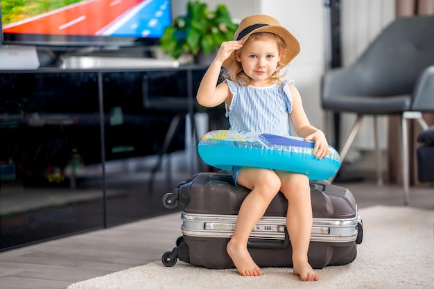 Mała dziewczynka z bagażem walizkowym i nadmuchiwaną boją ratunkową, gotowa do podróży na wakacje