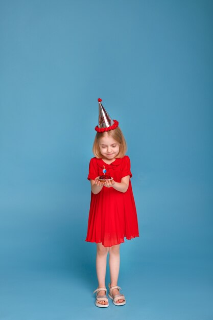 Mała dziewczynka z ciastem na jej urodziny na niebieskiej powierzchni