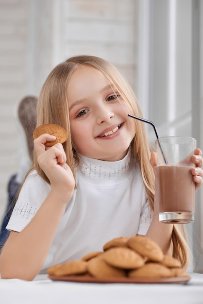 Mała dziewczynka z ciastkami i czekoladowym mlekiem