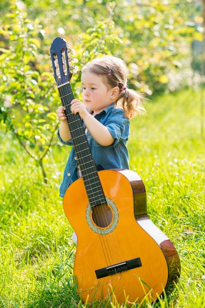 Mała dziewczynka z dużą gitarą akustyczną bawi się na zielonym trawniku