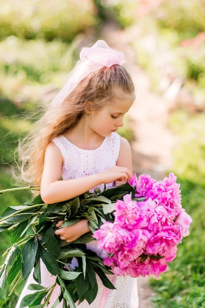 Zdjęcie mała dziewczynka z dużym bukietem piwonii. dziecko spaceruje po parku z kwiatami w lecie.