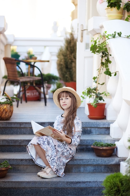 Mała dziewczynka z książką siedzi na schodach dziecko czyta książkę na świeżym powietrzu