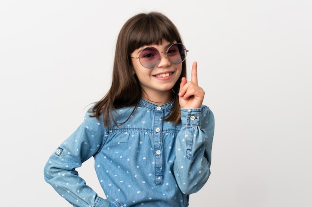 Mała dziewczynka z okularami przeciwsłonecznymi na białym tle pokazując i podnosząc palec na znak najlepszych
