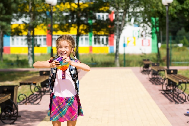 Mała dziewczynka z plecakiem i w szkolnym mundurku na szkolnym podwórku bawi się zabawką pop it.