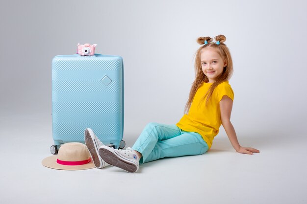 Mała dziewczynka z walizką podróżnika na białym tle