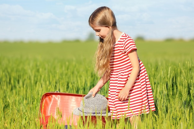 Mała dziewczynka z walizką w zielonym polu