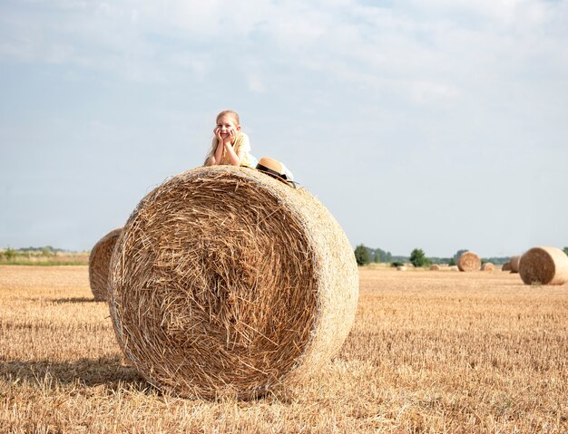 Mała dziewczynka zabawy w polu pszenicy w letni dzień. Dziecko bawiące się na polu beli siana w czasie żniw.
