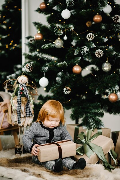 Mała dziewczynka zaskoczony Prezenty świąteczne na nowy rok Dziecko otwórz obecny prezent Wszystkiego najlepszego z okazji dziewczynka szuka magicznego pola Kid siedzi w pobliżu Xmas Tree