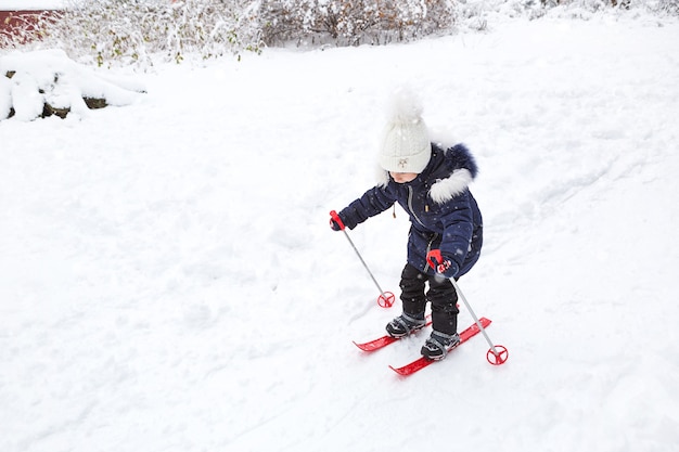 Mała dziewczynka zjeżdża po zboczu w czerwonych plastikowych nartach.