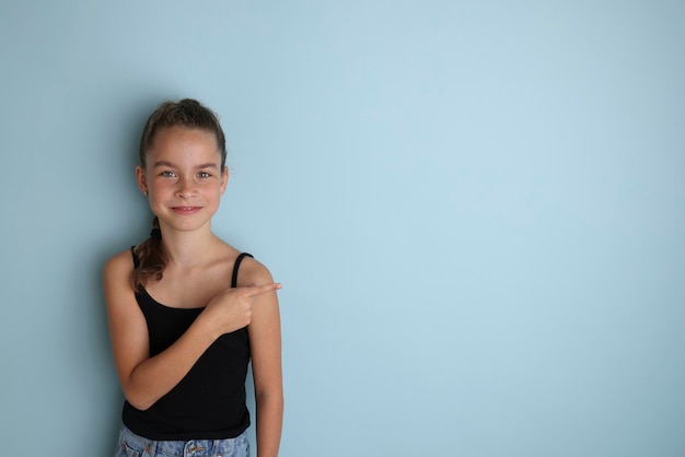 Mała emocjonalna nastolatka w czarnej koszulce w wieku 11 12 lat na odizolowanym niebieskim tle Portret studyjny dla dzieci Umieść tekst, aby skopiować miejsce na napis