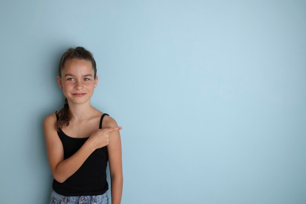 Mała emocjonalna nastolatka w czarnej koszulce w wieku 11 12 lat na odizolowanym niebieskim tle Portret studyjny dla dzieci Umieść tekst, aby skopiować miejsce na napis