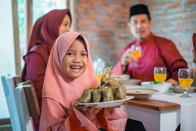 Mała indonezyjska dziewczyna w zasłonie uśmiecha się pokazując ketupat na talerzu