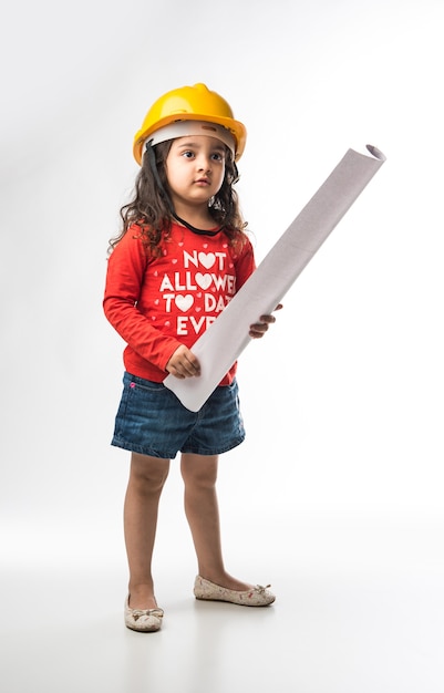 Mała indyjska dziewczyna inżynier z żółtym kaskiem i rolką papieru do rysowania lub planem, wyizolowana na białym tle