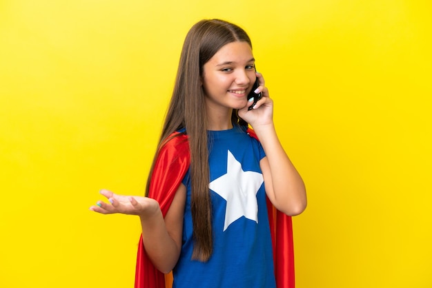 Mała kaukaska dziewczyna superbohatera odizolowana na żółtym tle, prowadząca rozmowę z telefonem komórkowym z kimś