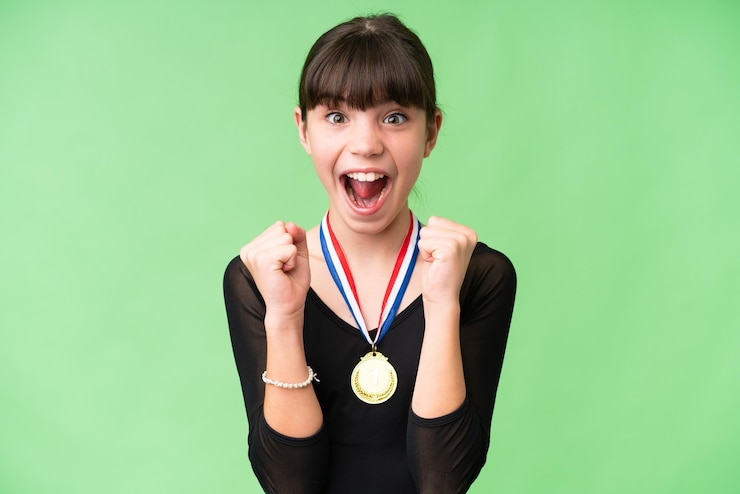 Zdjęcie mała kaukaska dziewczyna z medalami na odosobnionym tle świętuje zwycięstwo w pozycji zwycięzcy
