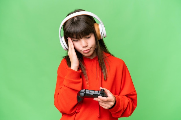 Zdjęcie mała kaukaska dziewczynka bawiąca się kontrolerem gier wideo na odizolowanym tle z bólem głowy
