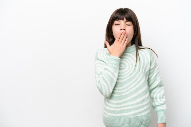 Mała kaukaska dziewczynka na białym tle ziewa i zakrywa ręką szeroko otwarte usta
