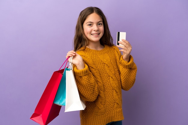 Mała kaukaska dziewczynka na fioletowym tle trzymająca torby na zakupy i kartę kredytową