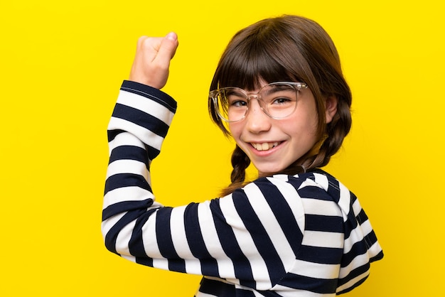 Mała kaukaska dziewczynka na żółtym tle w okularach i świętująca zwycięstwo