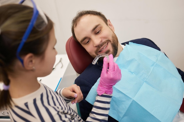 Zdjęcie mała kędzierzawa dziewczyna i jej ojciec bawią się w szczęśliwy związek dentysty